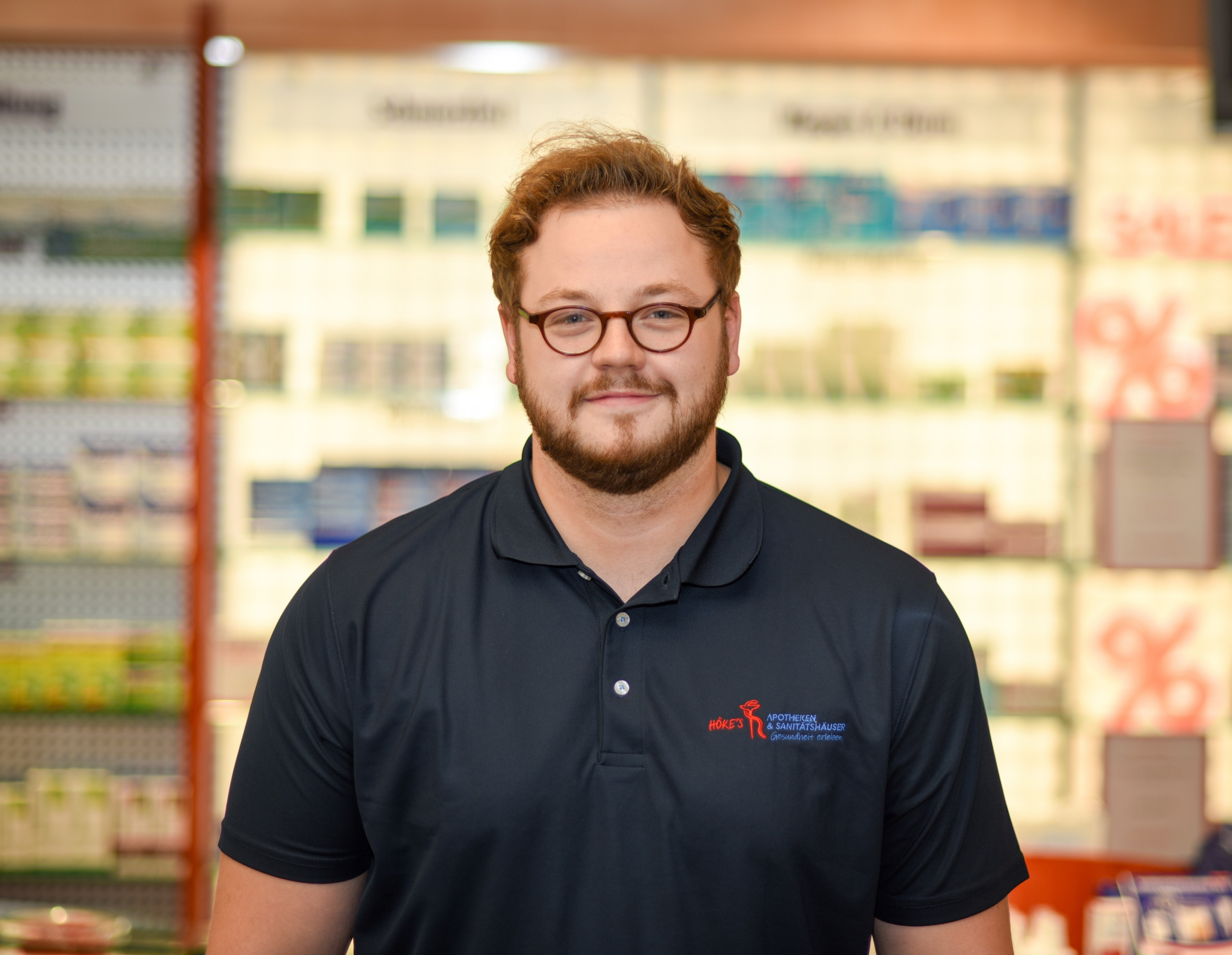 Alexander Scheele im Außendienst – Mitarbeiter der Höfer Apotheken Alexander Scheele im Außendienst, Mitarbeiter in Arbeitskleidung vor Apothekenregal