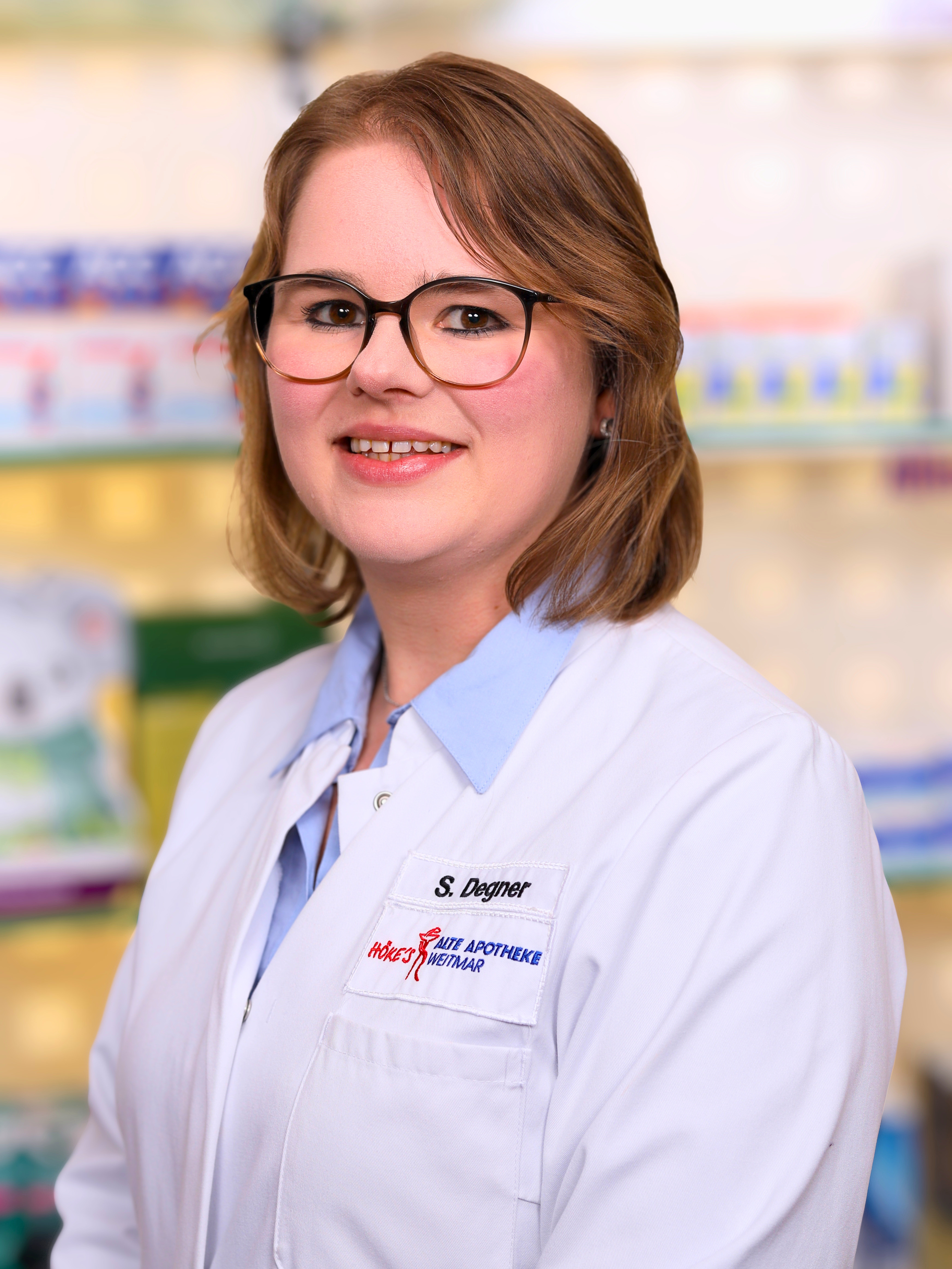 S. Degner, Mitarbeiterin der Alte Apotheke Wettmar, im weißen Kittel vor Apothekenregal