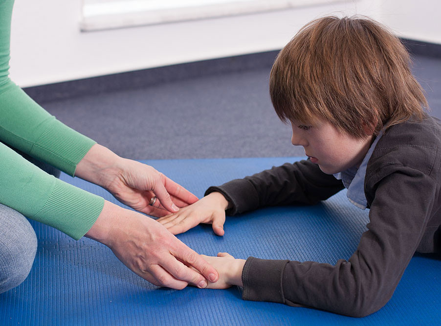 Ergotherapie: Behandlung eines Kindes auf blauer Matte Ergotherapie mit Kind, das auf blauer Matte liegt