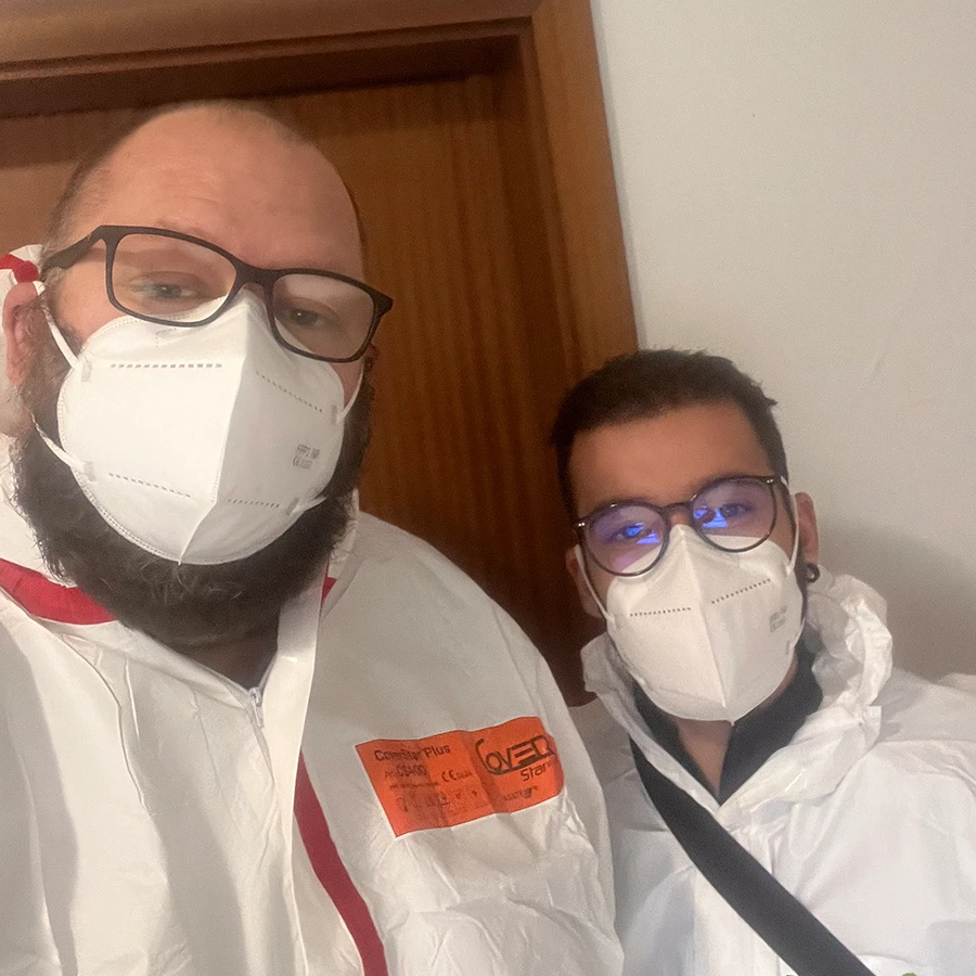 Zwei Personen in Schutzanzügen und Masken vor einer Holztür