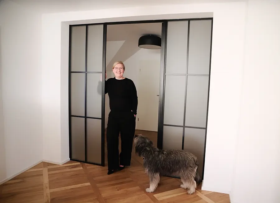 Jeanette Bazan Schmidt mit Hund vor einer modernen Glastür im Wohnzimmer