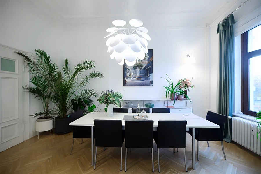 Moderner Sitzungsraum mit großem Tisch, schwarzen Stühlen, Pflanzen und Designerlampe