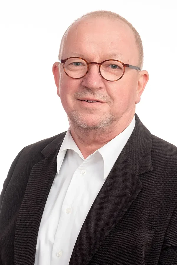 Porträt eines älteren Mannes mit Brille und Sakko vor weißem Hintergrund