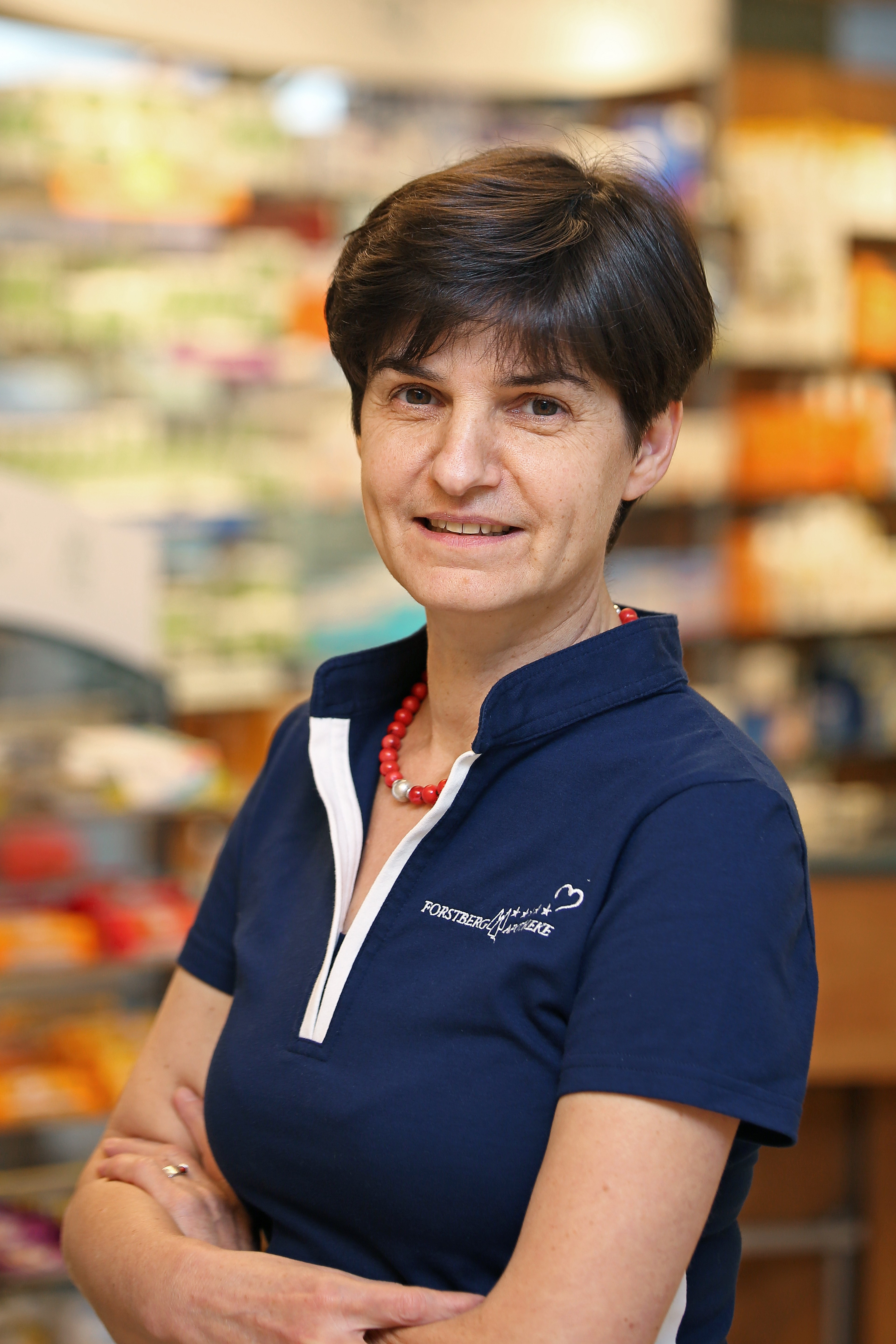 Frau in blauer Uniform mit roter Halskette in einer Apotheke