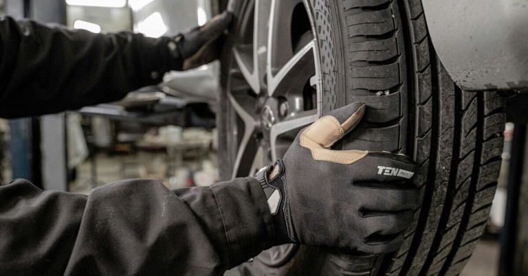 KFZ-Mechaniker bei der Reifenprüfung in der Autowerkstatt KFZ-Mechaniker prüft Reifen an einem Auto in der Werkstatt