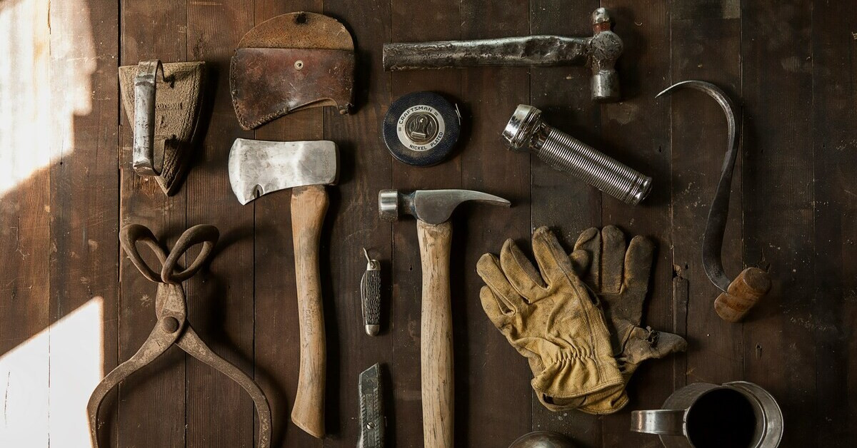 Werkzeuge sortiert auf rustikalem Holzboden – Hammer, Axt und Handschuhe Verschiedene Werkzeuge sortiert auf rustikalem Holzboden, darunter Hammer, Axt, Handschuhe und weitere Handwerksutensilien