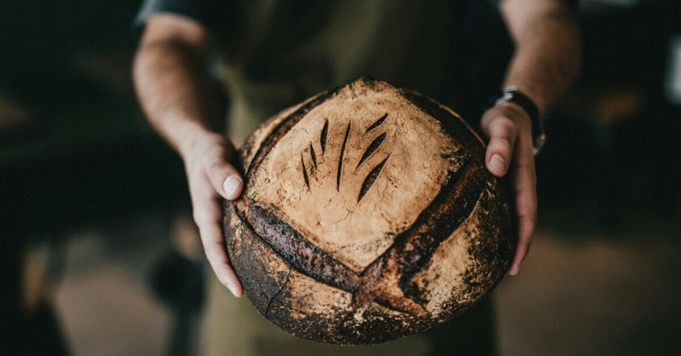 Bäcker mit Brot – frisch gebackenes Brot in den Händen eines Bäckers Bäcker hält frisch gebackenes Brot in den Händen
