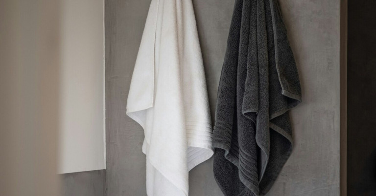 Aufgehängte Handtücher – weiße und graue Handtücher im Badezimmer Aufgehängte Handtücher in Weiß und Grau an einer Badezimmerwand
