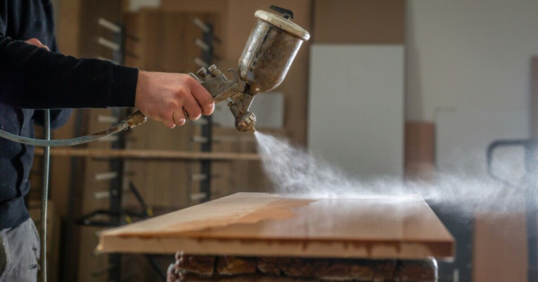 Holzplatte wird lackiert – Lackieren von Holz mit Sprühpistole Holzplatte wird mit einer Sprühpistole lackiert