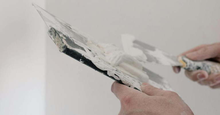 Riss mit Spachtelmasse füllen – Anleitung und Tipps zur Wandreparatur Riss mit Spachtelmasse füllen – Hand hält Spachtel mit weißer Spachtelmasse vor einer Wand