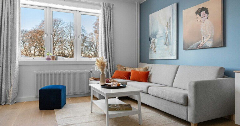 Modernes blaues Wohnzimmer mit grauem Sofa, weißen Möbeln und großen Fenstern