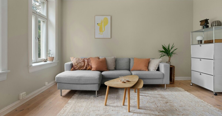 Modernes Wohnzimmer mit sandfarbener Wand, grauem Sofa und Holztisch