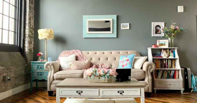 Gemütliches grünes Wohnzimmer mit beigem Sofa, dekorativen Kissen und Blumen auf dem Couchtisch