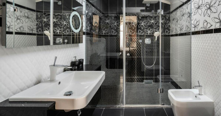 Moderne ebenerdige Dusche mit Sitzbank in einem stilvollen Badezimmer mit schwarzer Fliesenoptik und floralen Mustern.