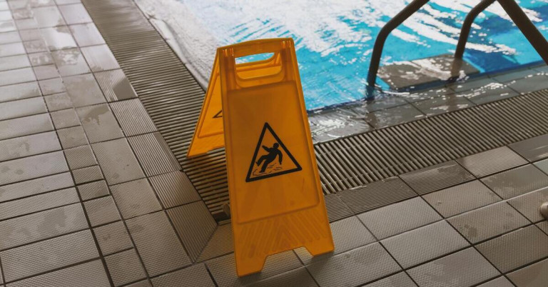 Rutschsichere Fliesen vor einem Swimming Pool mit Warnschild gegen Ausrutschen