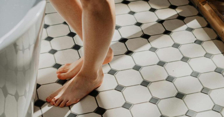 Frau steht barfuß vor der Badewanne auf Fliesenboden im Badezimmer