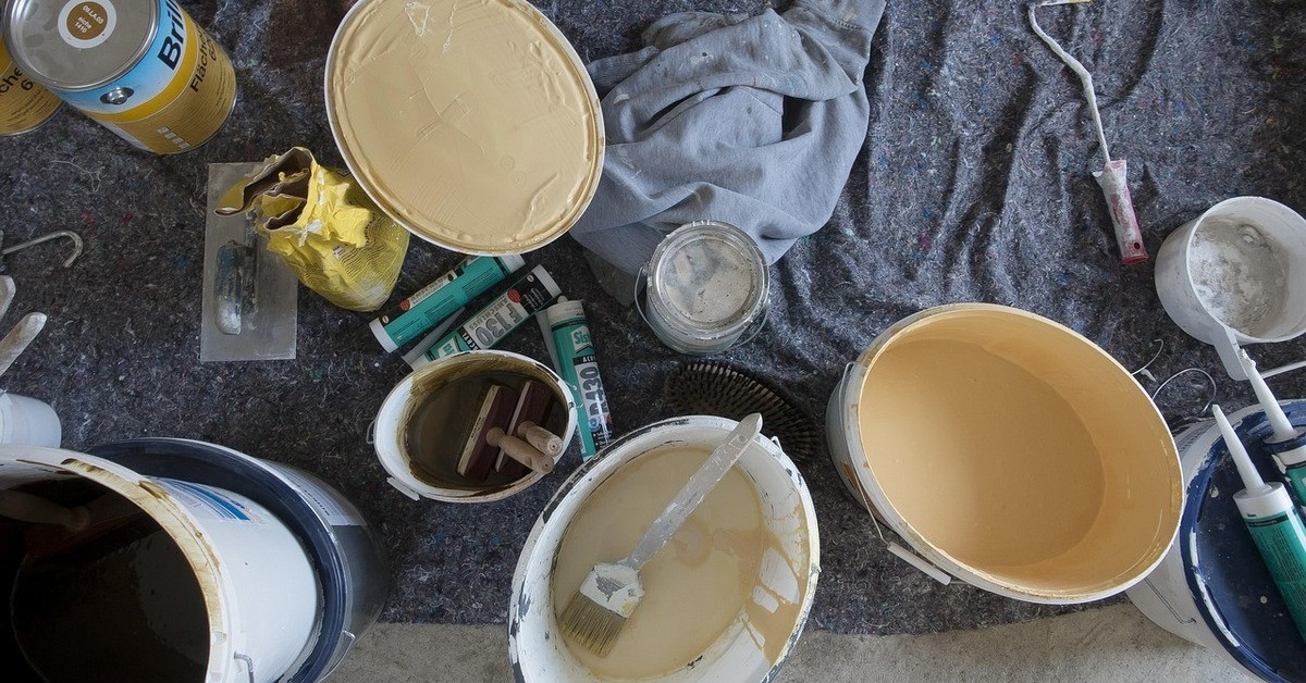 Farbeimer und Pinsel auf einer Abdeckplane, Malerutensilien für Renovierungsarbeiten