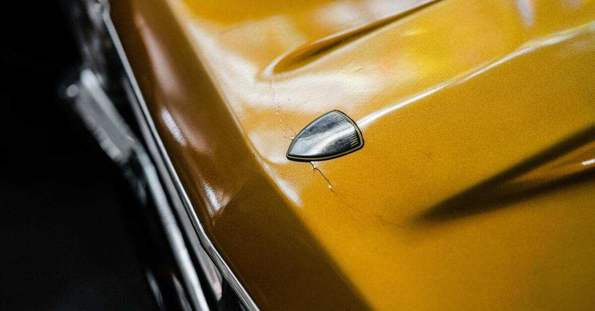 Lackschaden auf gelbem Auto, Nahaufnahme mit sichtbaren Rissen im Lack