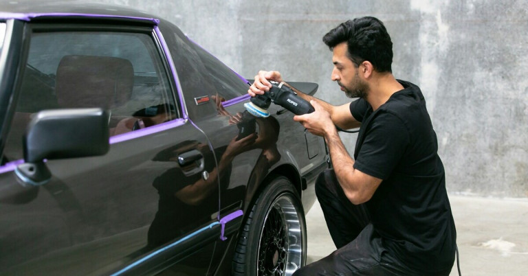 Mann poliert Autolack mit einer Poliermaschine in einer Werkstatt