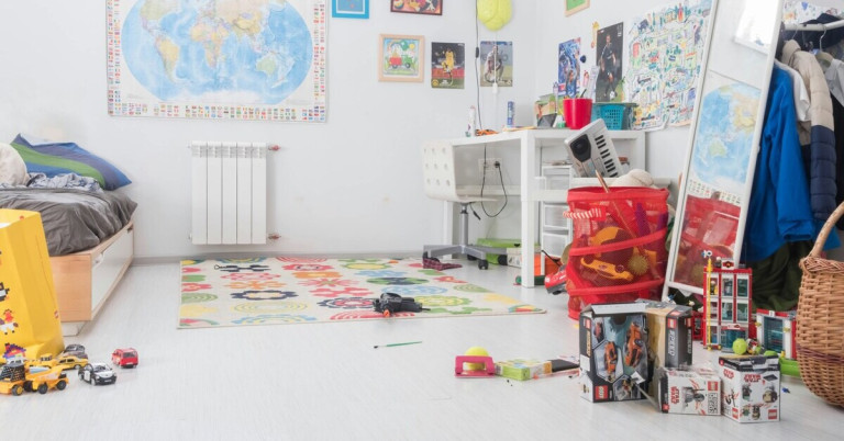Kinderzimmer mit Schreibtisch in der Ecke, buntem Teppich und Spielzeug auf dem Boden