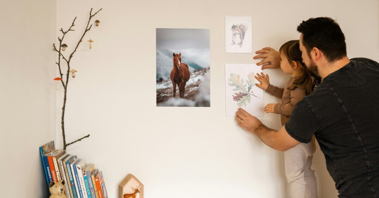 Zwei Personen hängen Wandbilder mit Tier- und Naturmotiven an eine helle Wand auf