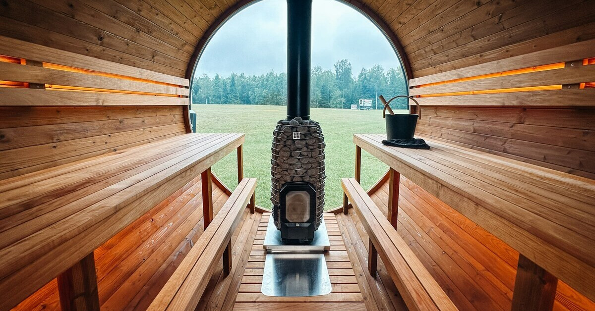 Innenansicht einer Fasssauna mit Holzofen und Blick ins Grüne