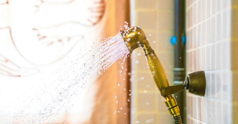 Warmwasser aus einer Dusche mit goldener Brause im Badezimmer
