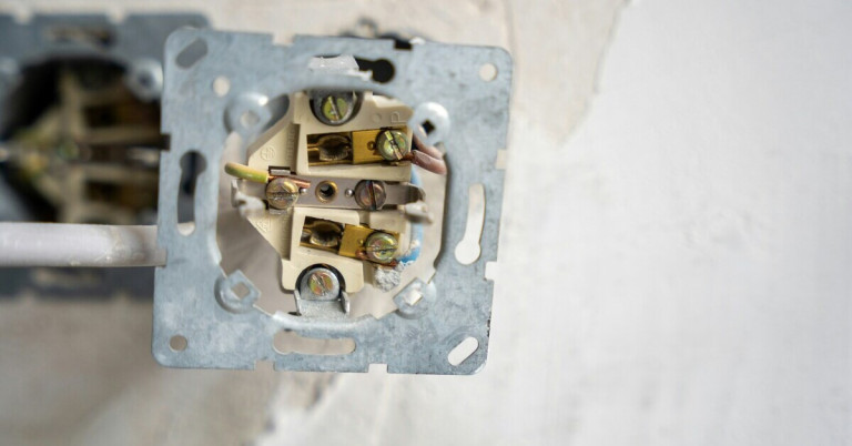 Offene Steckdose mit sichtbarer Verdrahtung in einer Wand