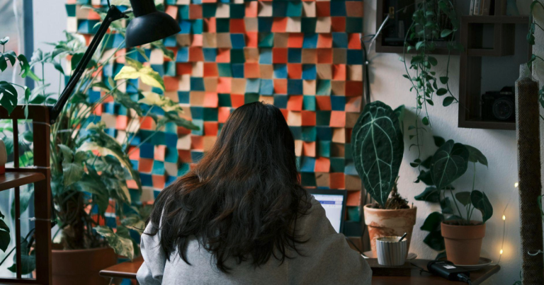 Frau arbeitet an einem kreativen Arbeitsplatz mit buntem Wanddekor und Pflanzen