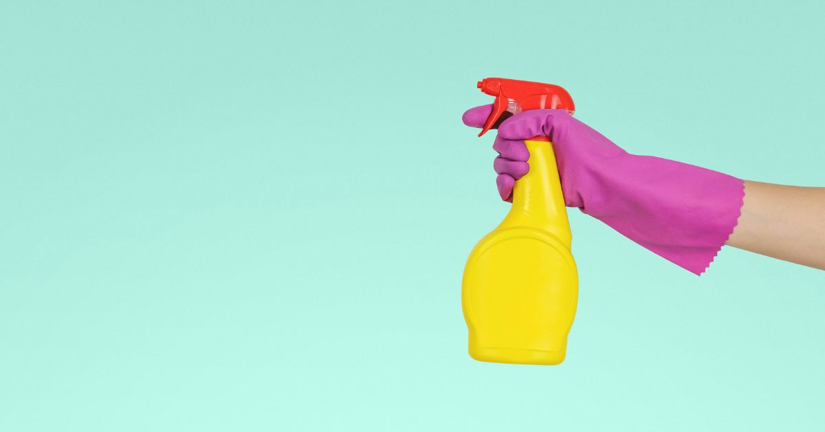 DIY Putzmittel in gelber Sprühflasche mit lila Handschuh vor türkisfarbenem Hintergrund