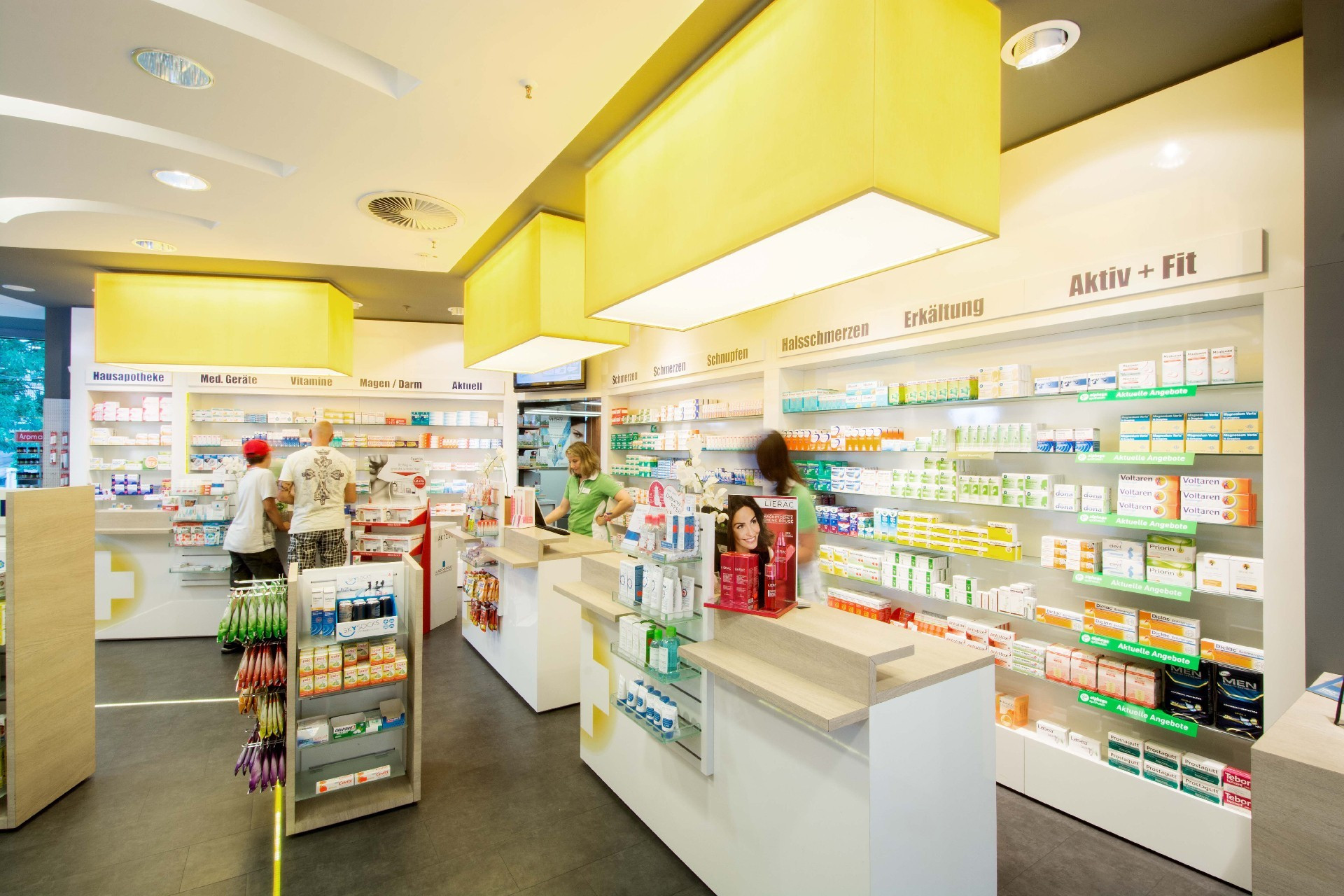 Innenansicht einer Apotheke mit Regalen voller Medikamente und Kunden