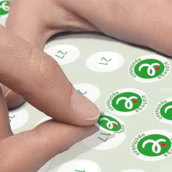 Hand klebt Apotheken-Aufkleber auf ein Blatt.