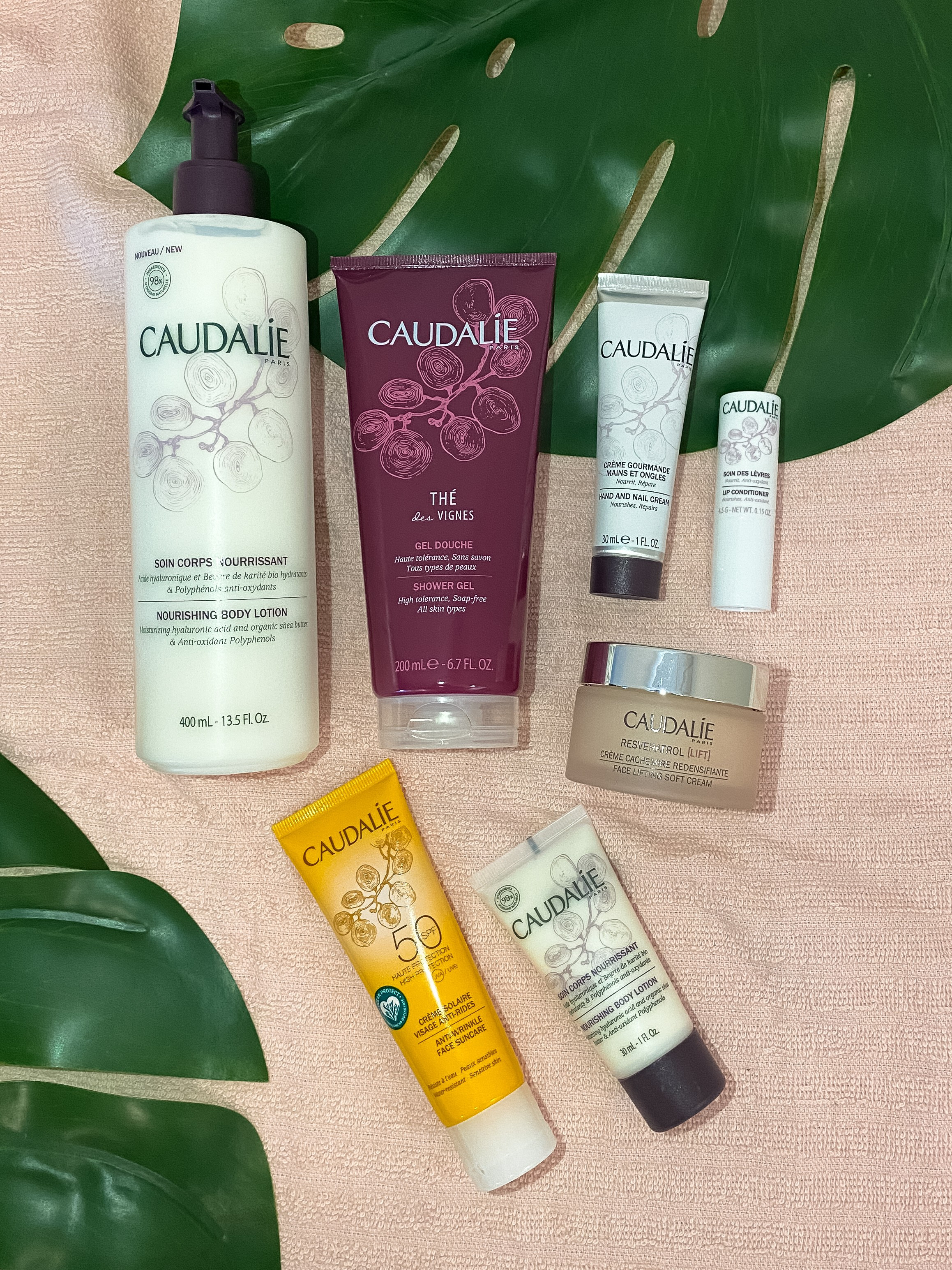 Caudalie Produkte auf einem rosa Hintergrund mit grünen Blättern