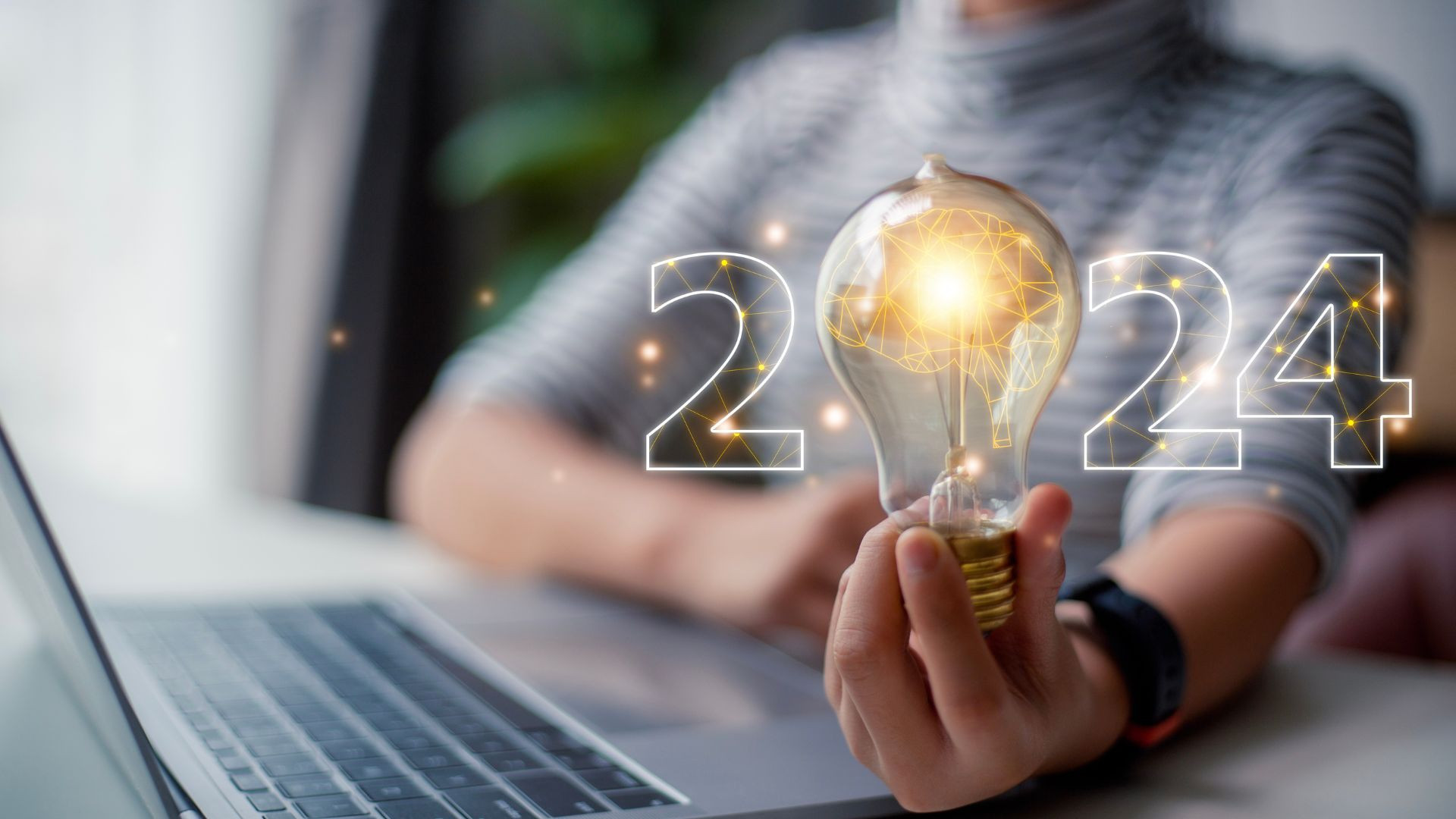 Person hält Glühbirne vor Laptop mit 2024 im Hintergrund, symbolisiert Marketing-Trends