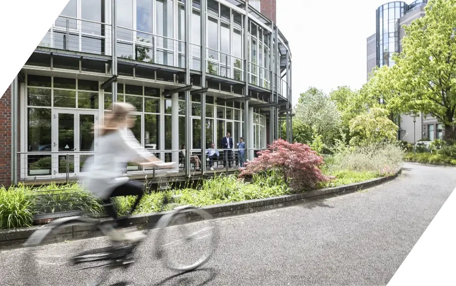 Person fährt mit dem Fahrrad vor einem modernen Bürogebäude
