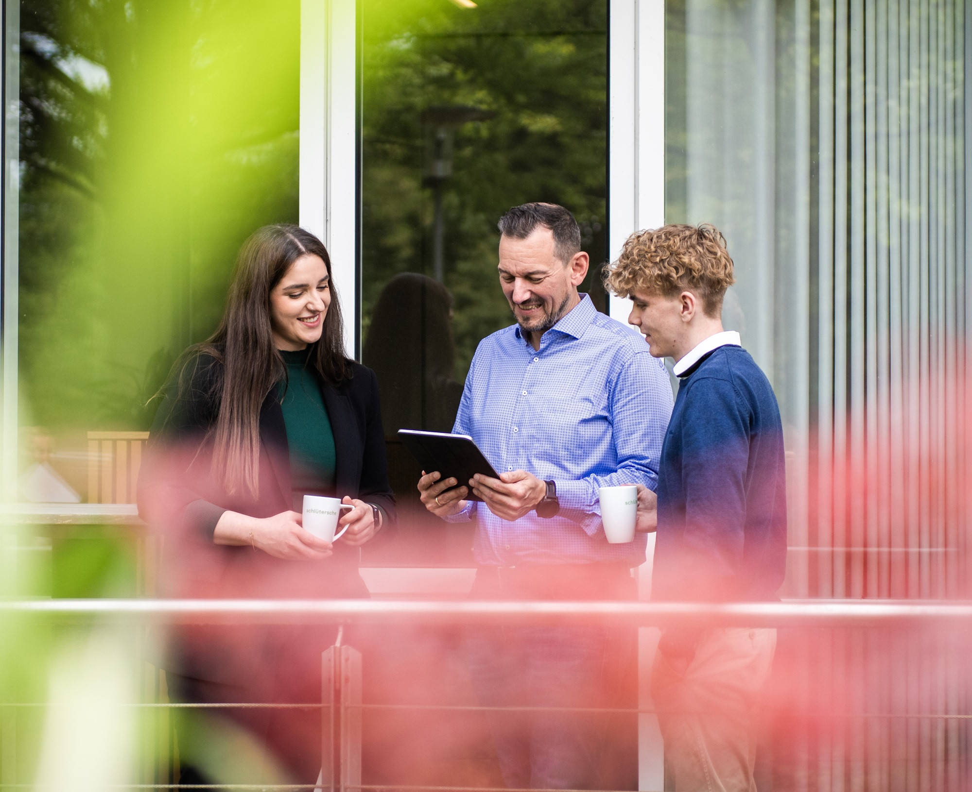 Drei Personen bei einem Team-Meeting im Freien mit Tablet und Kaffeetassen