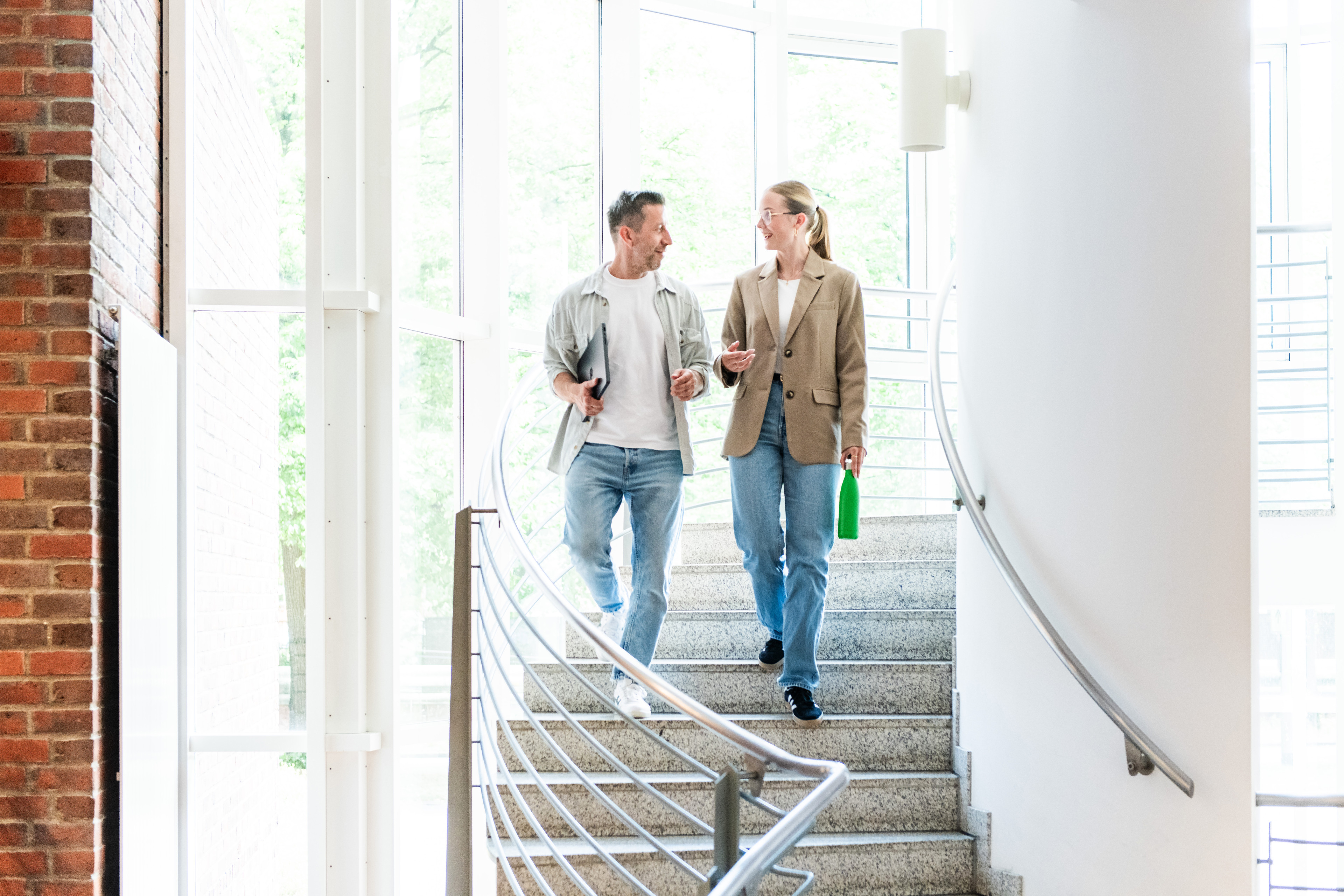 Zwei Büroangestellte im Gespräch auf einer Treppe in einem modernen Bürogebäude.