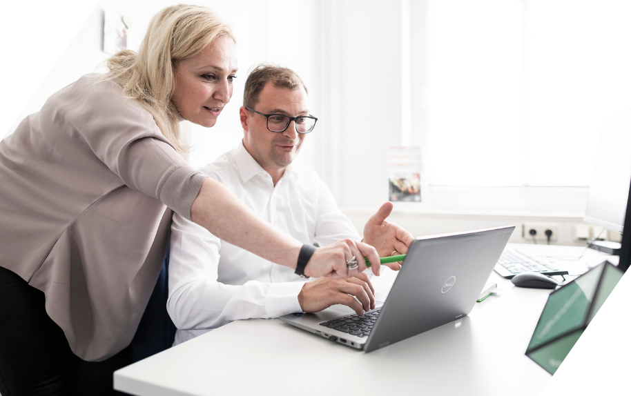 Zwei Personen arbeiten gemeinsam an einem Laptop im Büro.