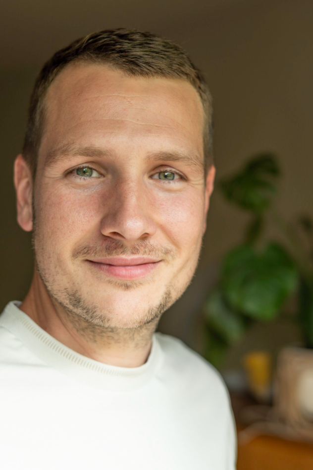Porträt eines Mannes in weißem Pullover vor unscharfem Hintergrund, aufgenommen am 10. September 2025
