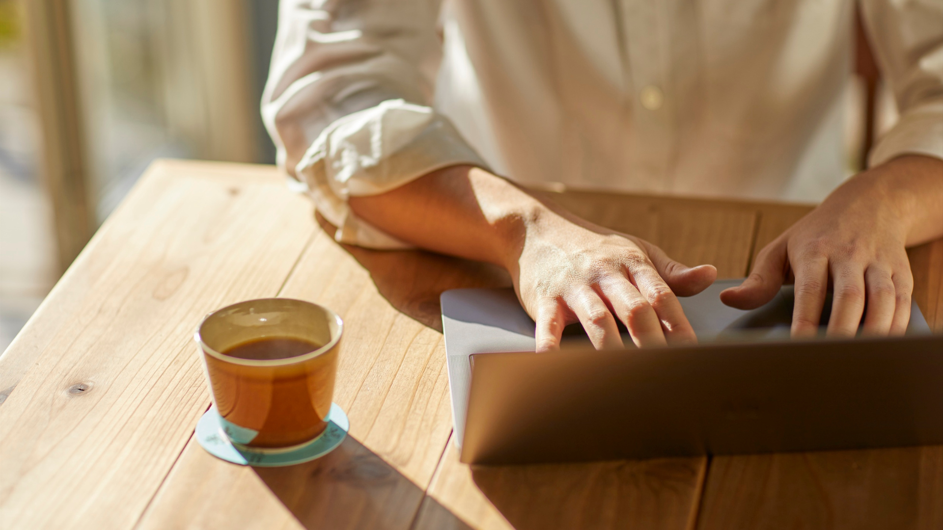 Person recherchiert am Laptop zu Suchmaschinenoptimierung FAQ bei einer Tasse Kaffee