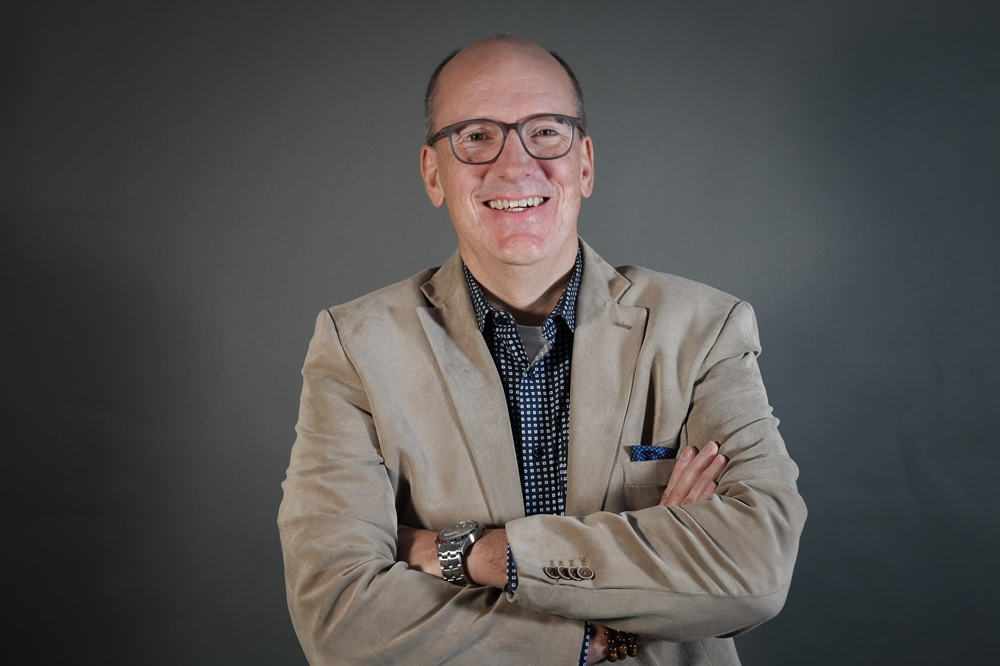 Christian Linde im beigen Sakko mit verschränkten Armen vor grauem Hintergrund