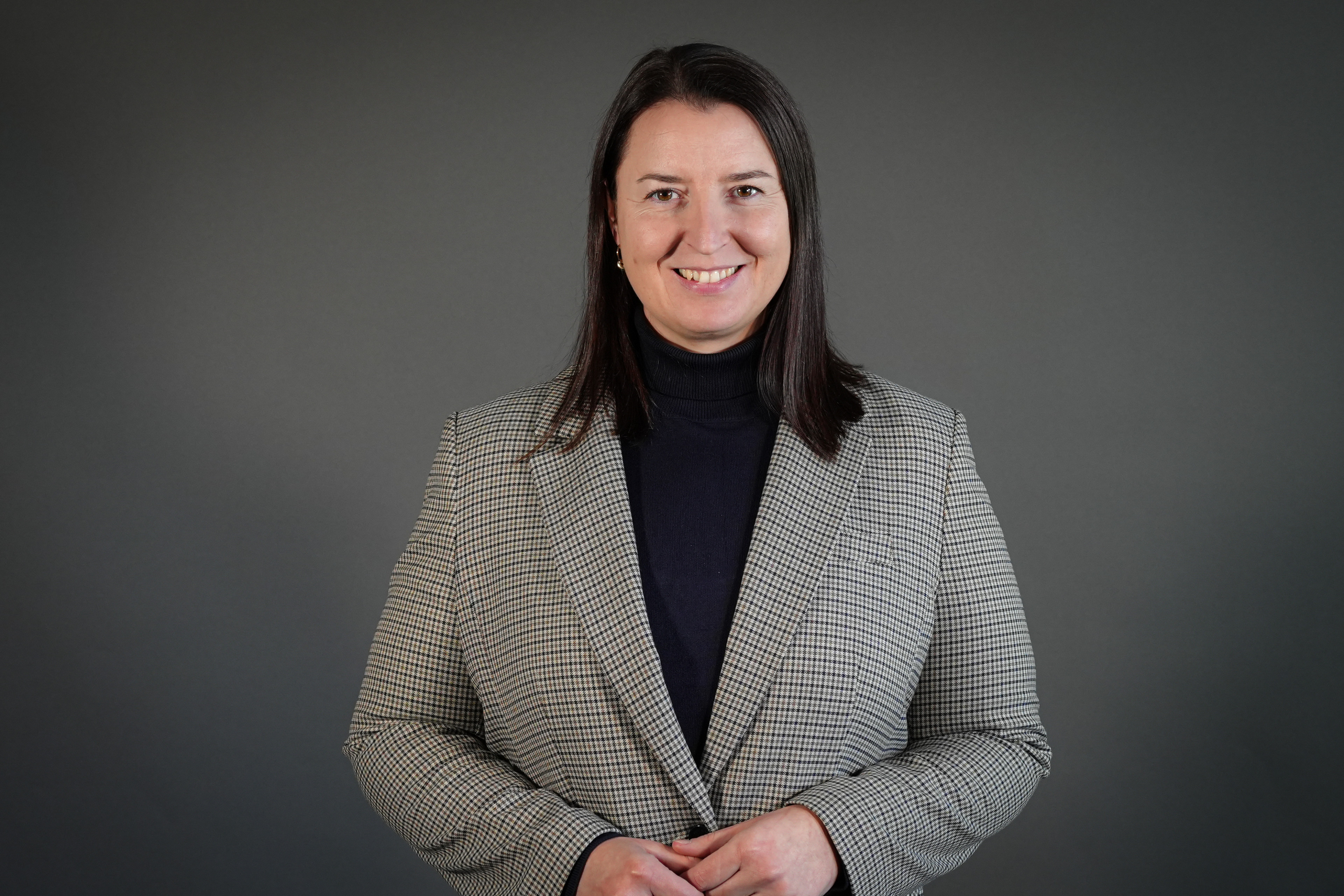 Roksana im karierten Blazer vor grauem Hintergrund