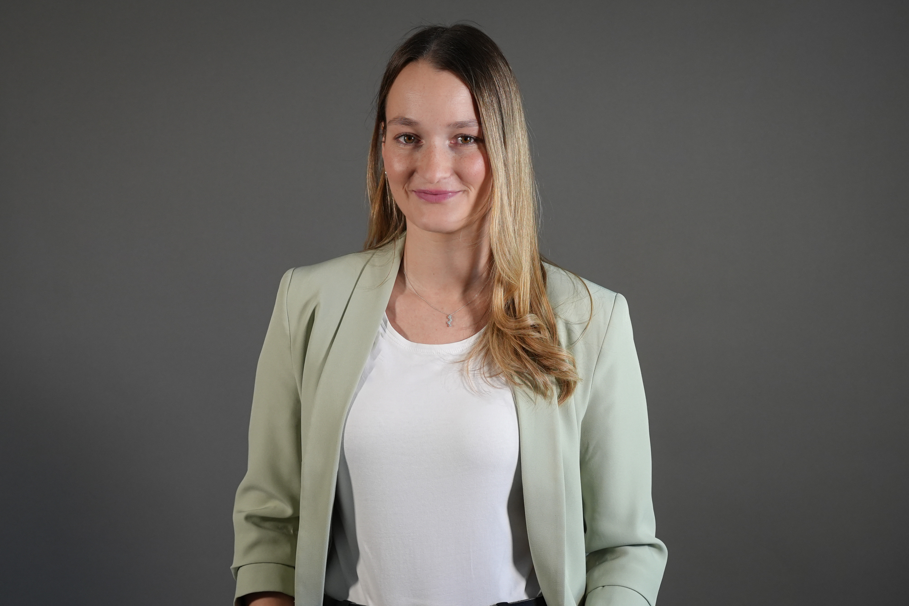 Alicia im Business-Outfit mit hellgrünem Blazer vor grauem Hintergrund