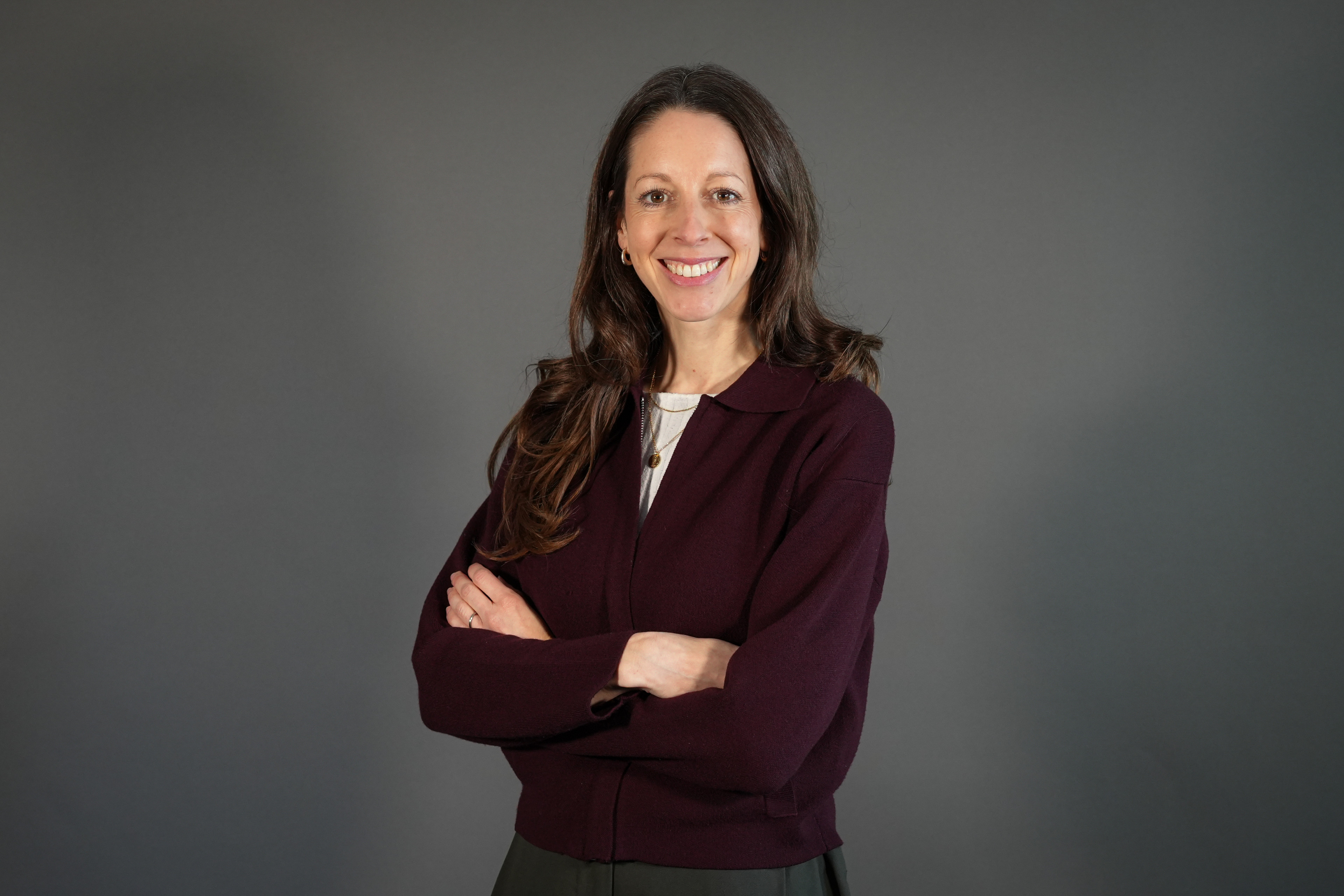 Frauke mit langen braunen Haaren und burgunderroter Jacke vor grauem Hintergrund