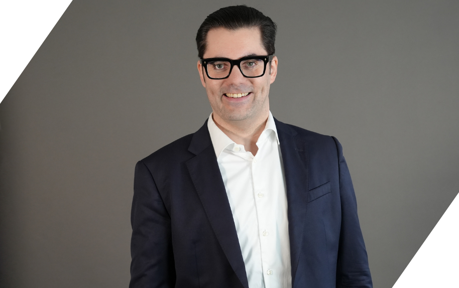 Marco Quer im Business-Outfit vor grauem Hintergrund