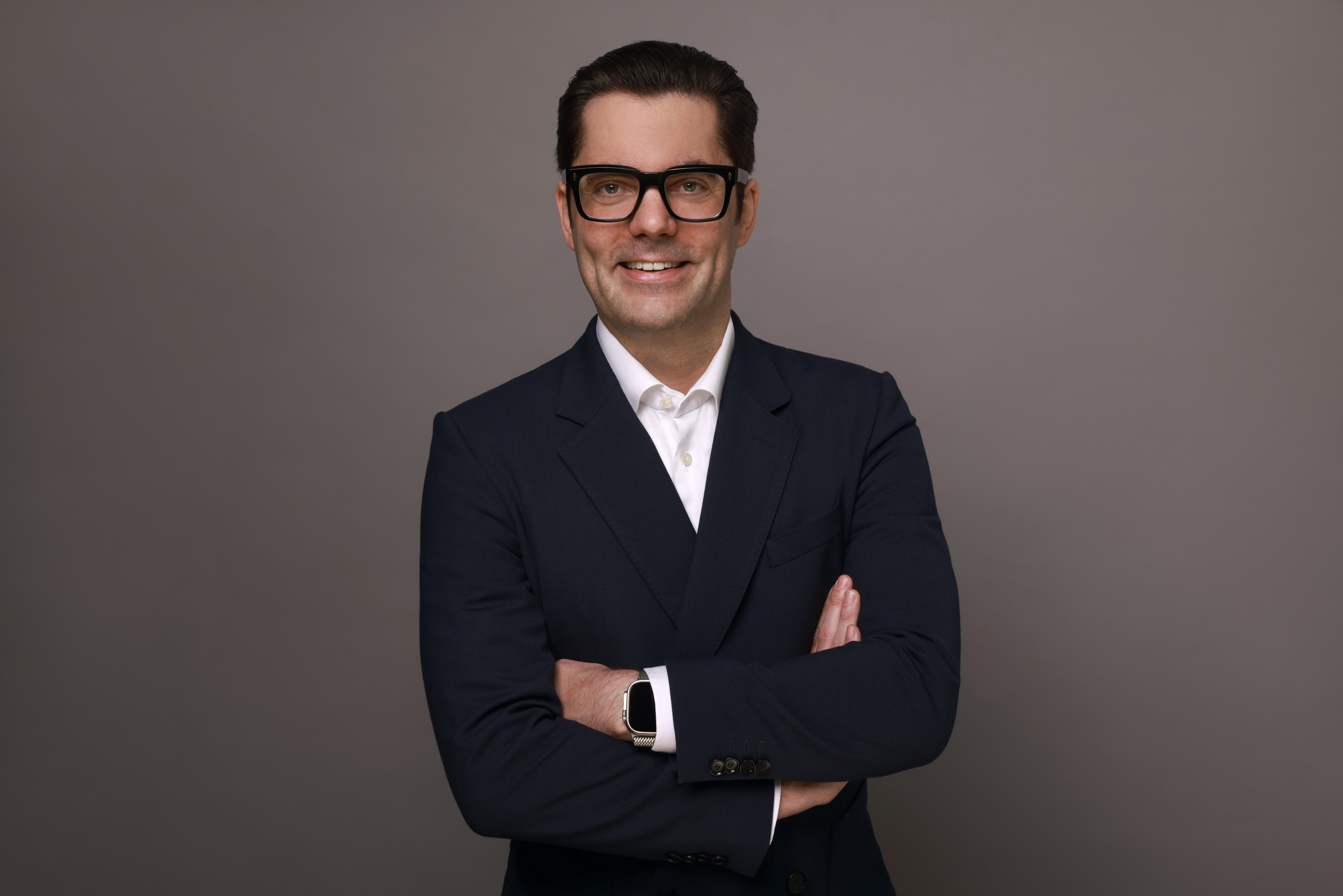 Geschäftsmann im Anzug mit verschränkten Armen vor grauem Hintergrund