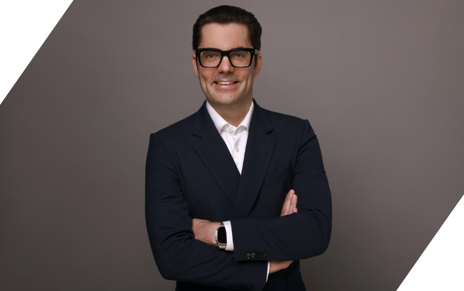 Marco im Business-Outfit mit verschränkten Armen vor grauem Hintergrund