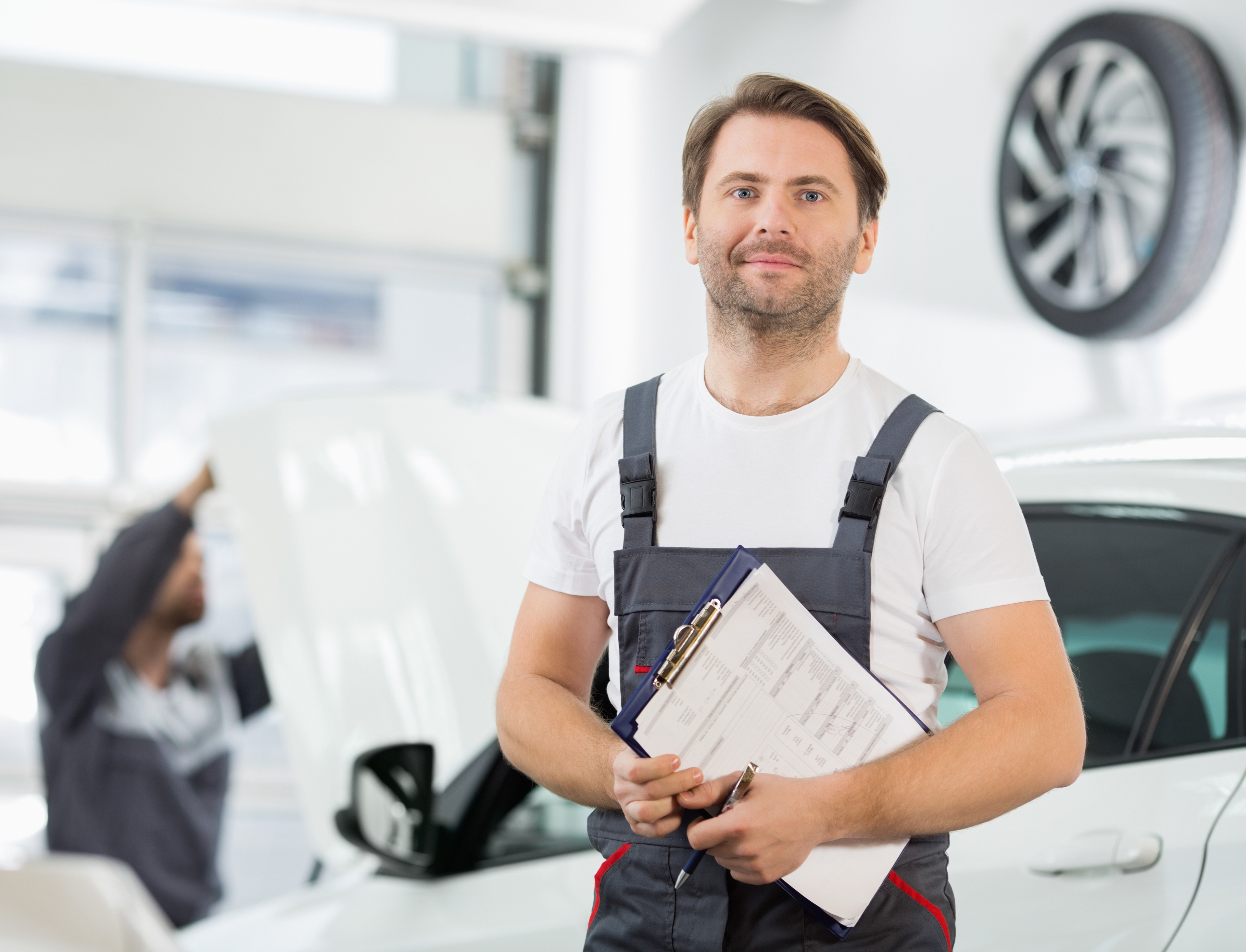 Kfz-Mechaniker mit Klemmbrett in einer Autowerkstatt vor einem Auto