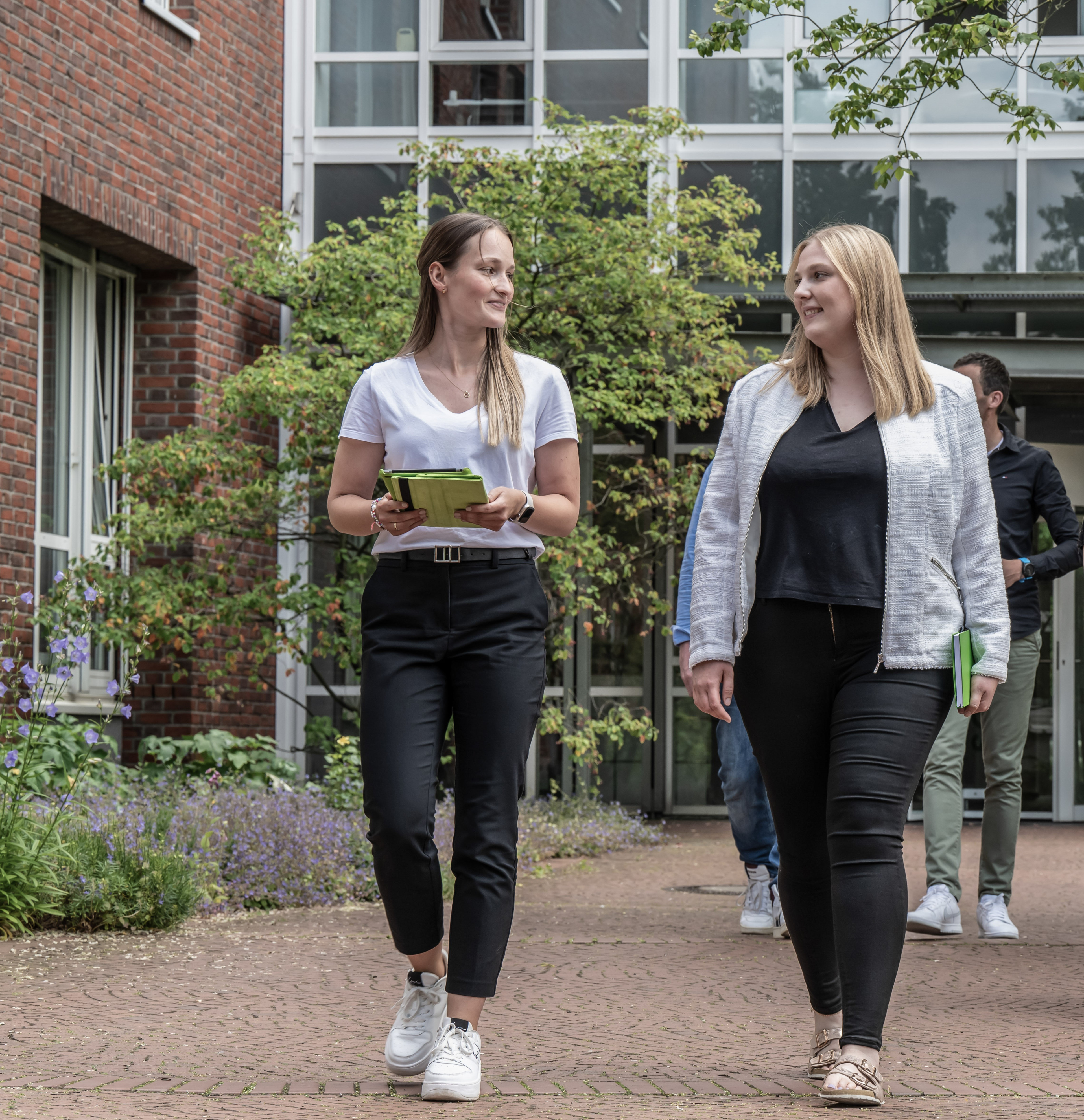 Studierende gehen auf dem Campus einer Hochschule im Sommer 2023