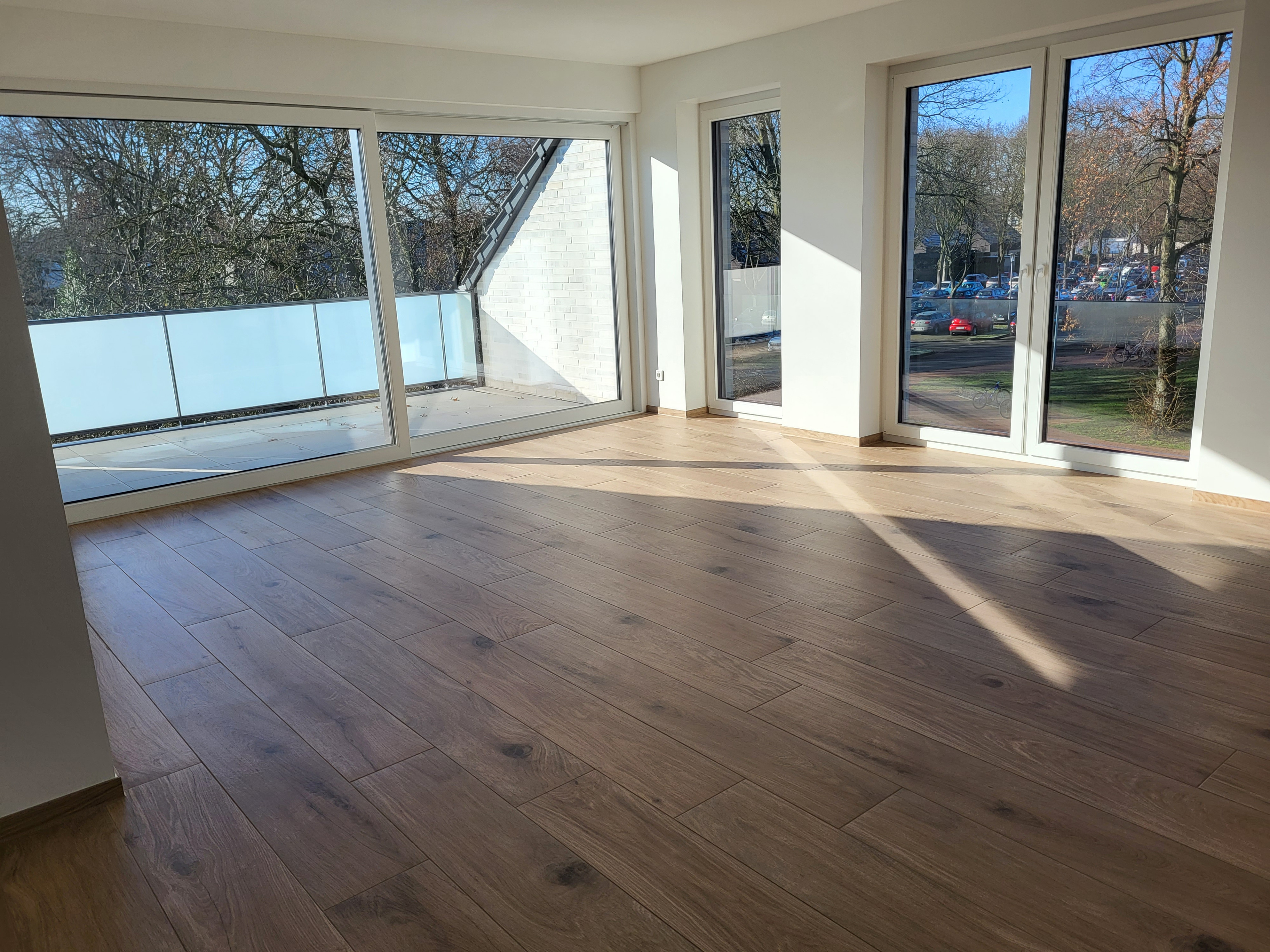 Helles Wohnzimmer mit großem Fenster und modernem Holzfußboden, Sonnenlicht fällt in den Raum